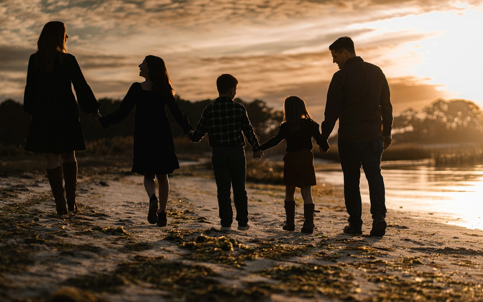 A family of five holding hands on a beach at sunset
