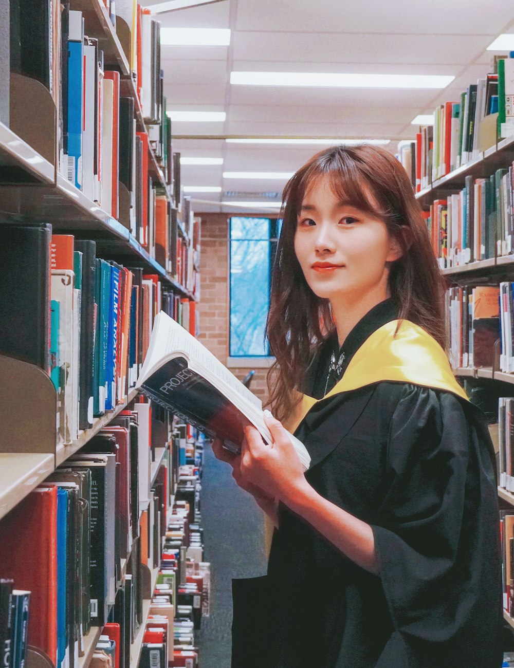 A graduate in her gown smiling in a university library