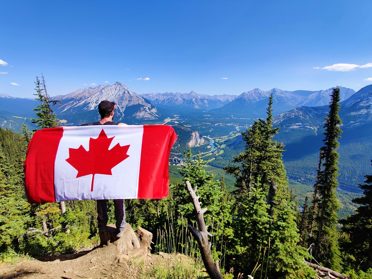 A young man holding a Canadian flag above the mountains