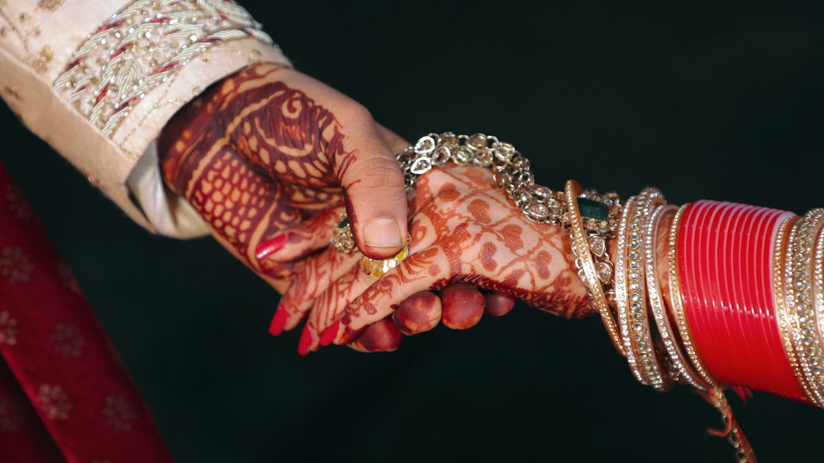 A bride with henna and bangles holding hands with her husband