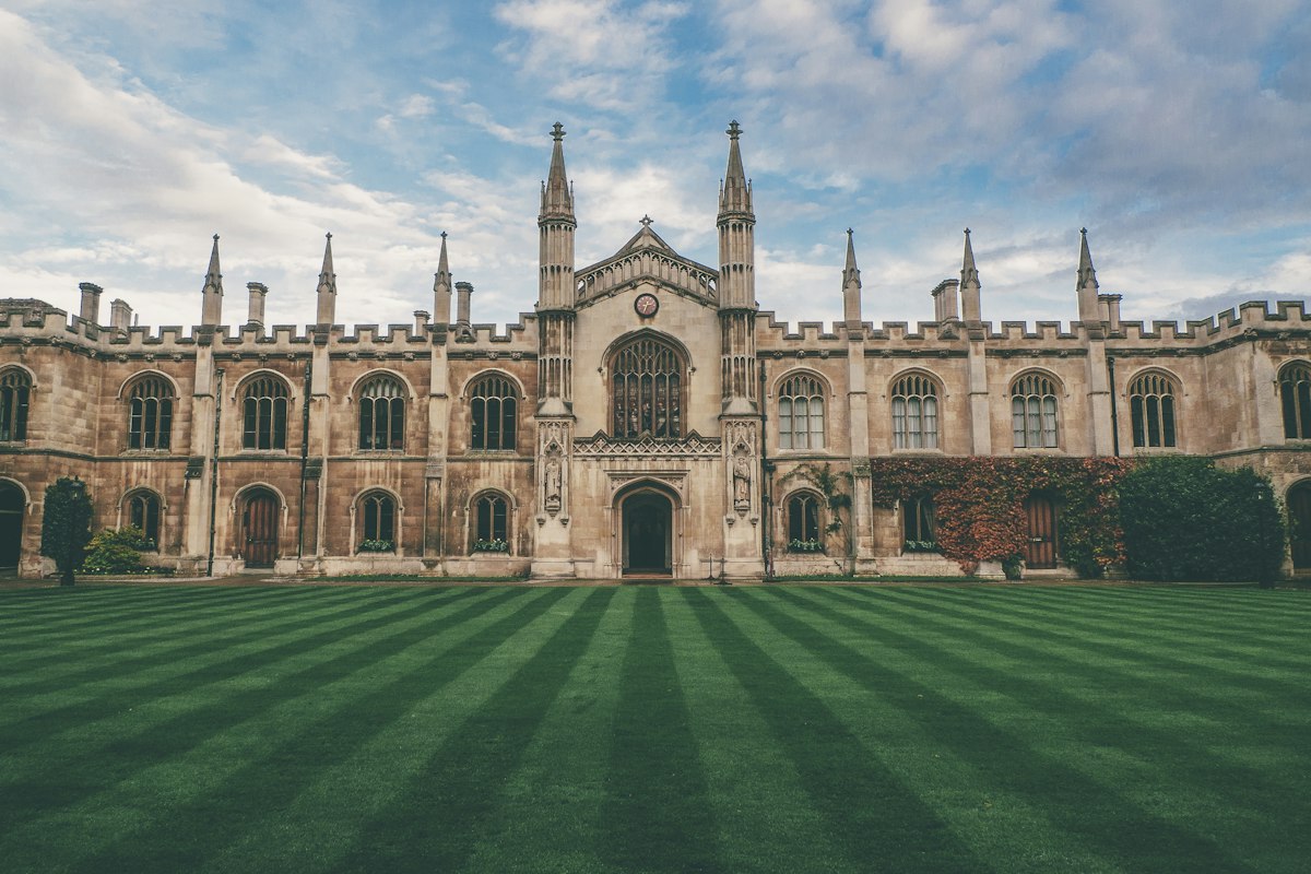 A historic college building and lawn in Cambridge under a blue sky