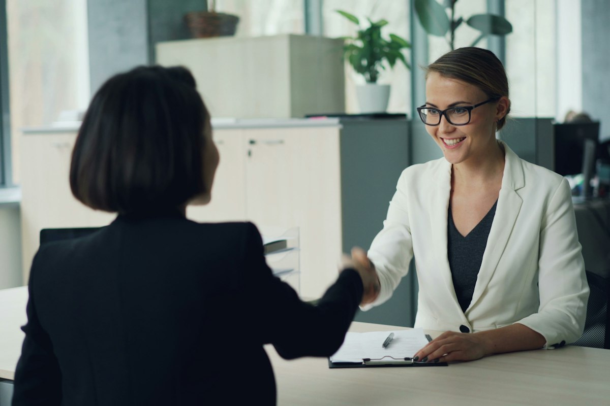 Two people shaking hands across a desk at an interview