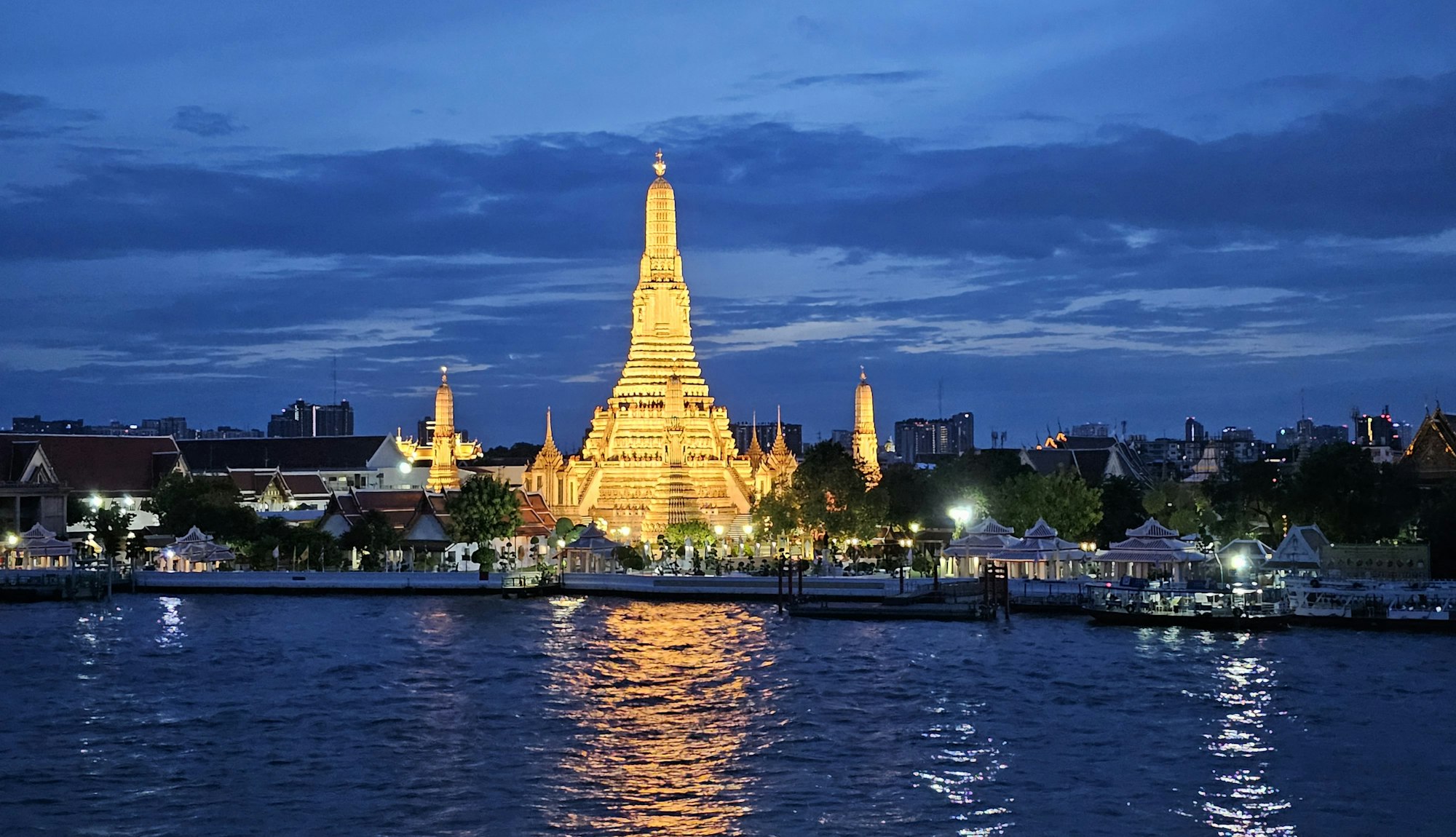 Wat Arun temple lit up at blue hour beside the river in Bangkok