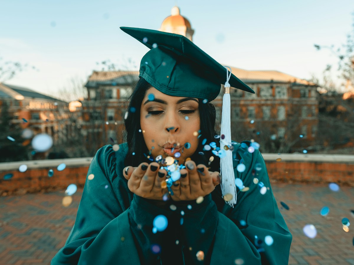 A graduate blowing confetti in cap and gown