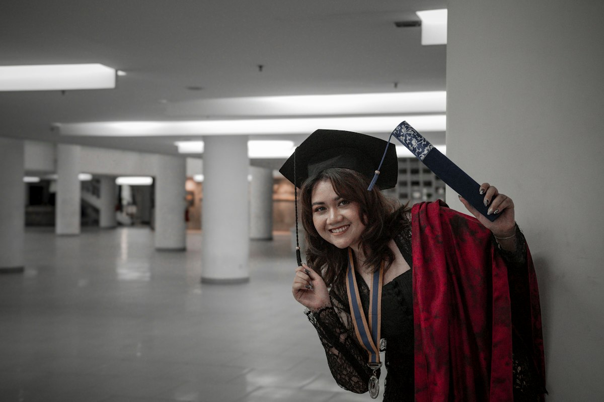 A young woman in a graduation gown waving happily, the result a well read decision letter can still lead to