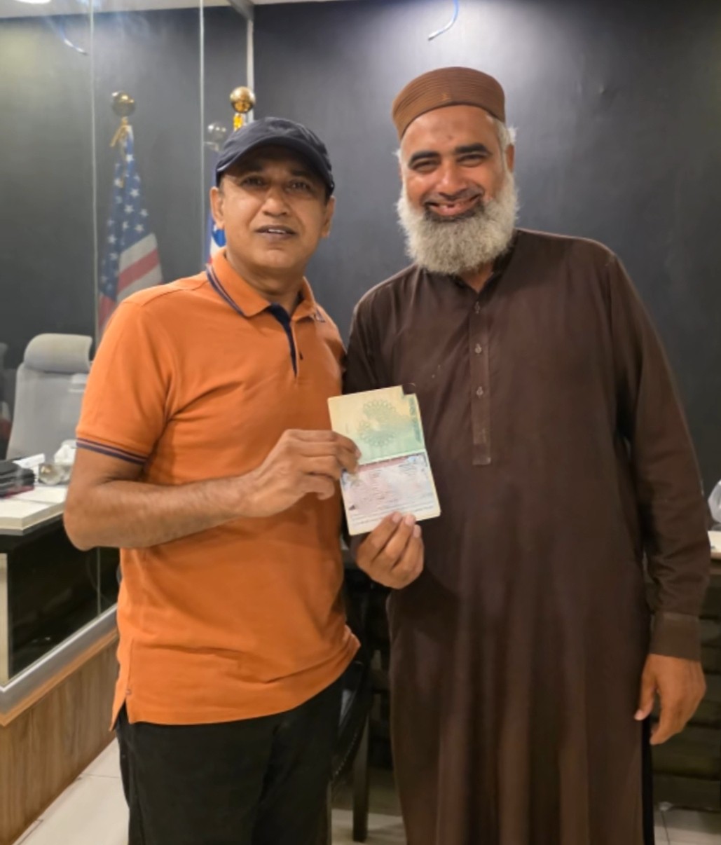 Allah Ditta holding his passport with his new US IR1 visa, standing with Mujtaba Maharvi at the Westside office in DHA Lahore