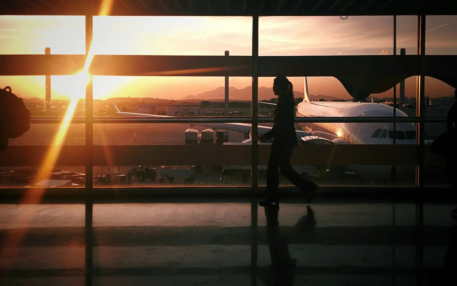 A traveller at an airport window at sunset, watching a plane
